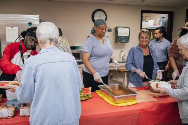 Four people standing at a table serving food to older adults 