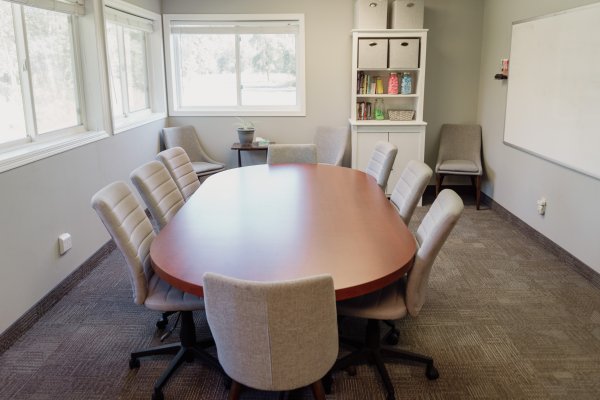 A conference room with a large oval table surrounded by office chairs and a white board on right wall