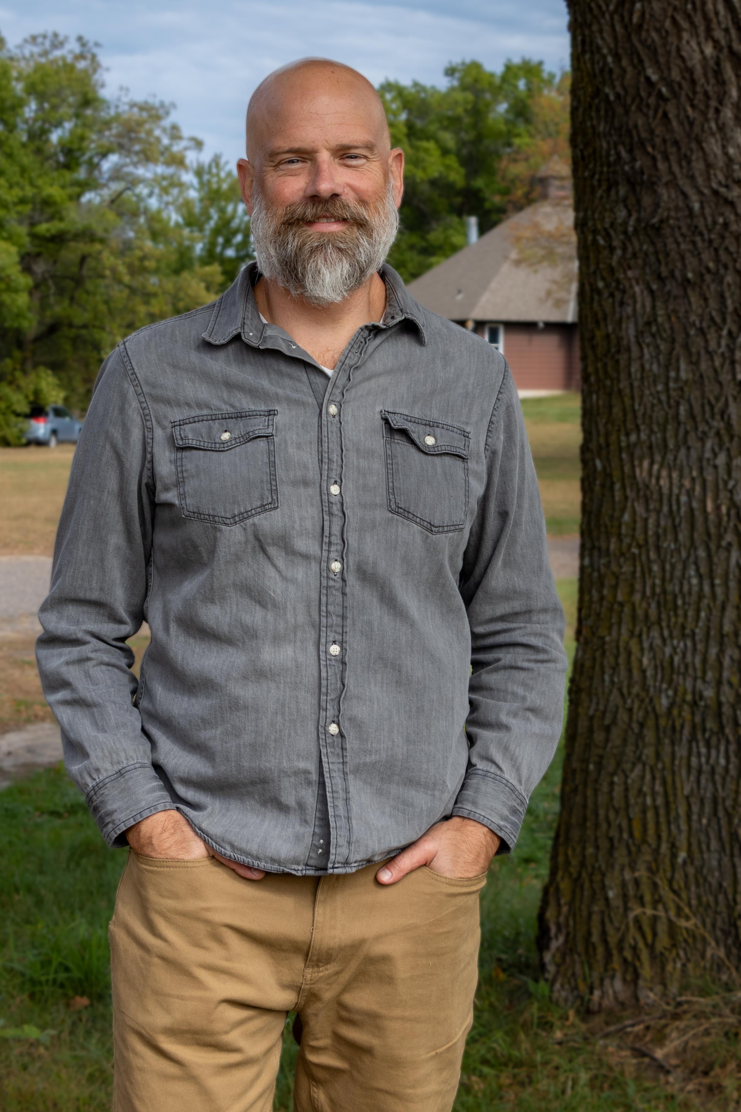 a man with his hands in his pockets standing outside next to a tree