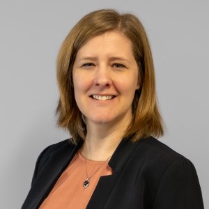 A woman with shoulder-length smiling in front of a gray wall.