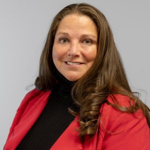 A woman smiling with long brown hair wearing a red blazer over a black turtleneck