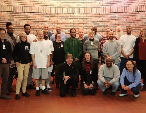A group photo of diverse individuals smiling and posing in front of a brick wall