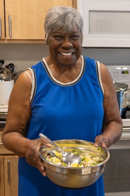 an older woman holding a bowl of salad greens