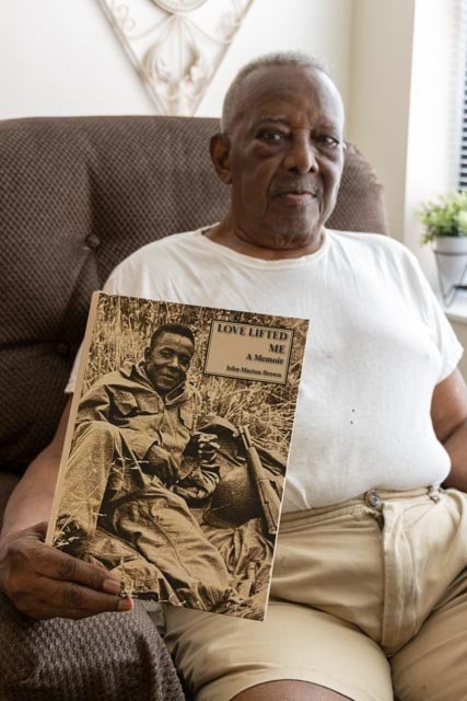 an older man sitting in a chair holding a book up 