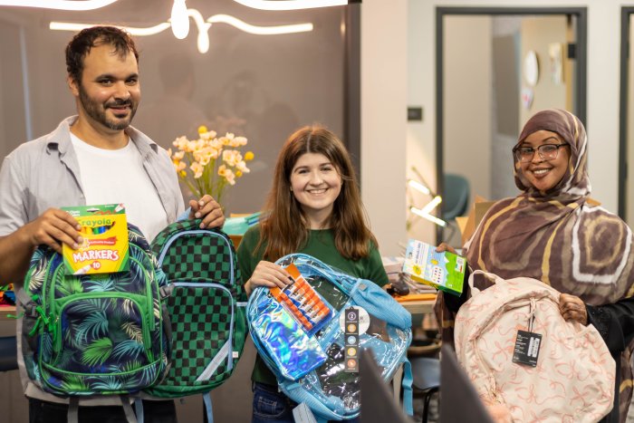 Three VOA staff members hold backpacks and smile