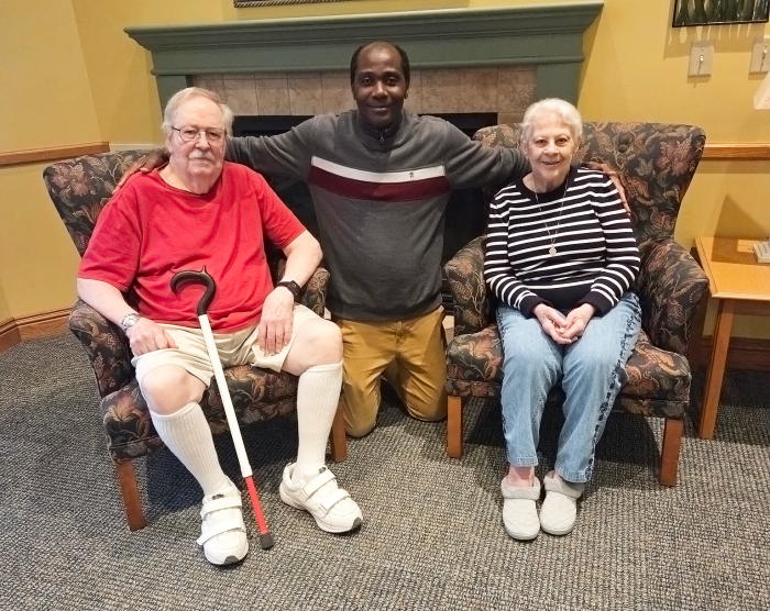 a man kneeling towards the camera between two older adults sitting in chairs smiling