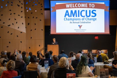 An audience of people sitting at tables listening to a women speaking at a podium