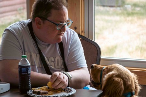 a young man sitting in a chair and looking at the dog sitting next to him