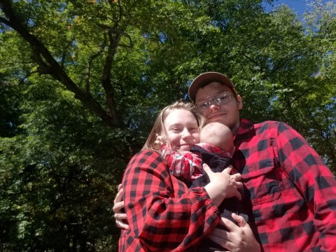 a young man and woman standing outside holding a baby