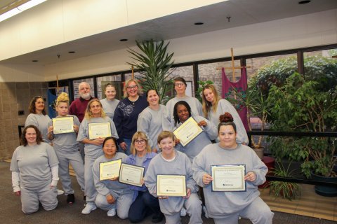a group of women holding up certificates indoors, some kneeling and some standing