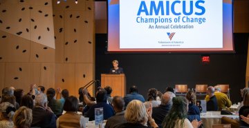 An audience of people sitting at tables listening to a women speaking at a podium