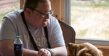 a young man sitting in a chair and looking at the dog sitting next to him