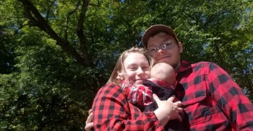 a young man and woman standing outside holding a baby