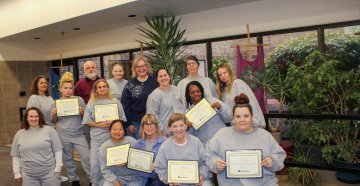 a group of women holding up certificates indoors, some kneeling and some standing