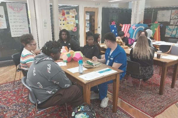 Students and teachers sit together at tables in a large classroom