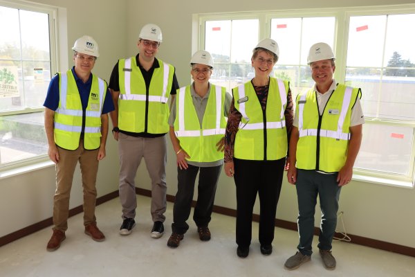 a group of five individuals standing in an empty room wearing construction hats