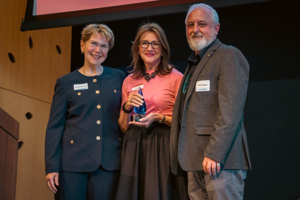 A woman standing on stage holding an award between a woman and man