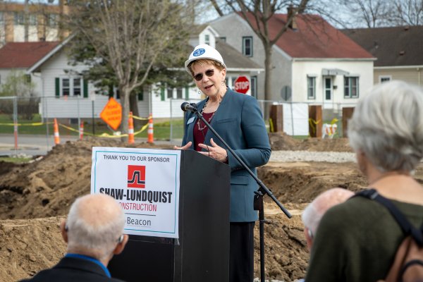 Woman outside at a podium with a construction hat on speaking to a crowd