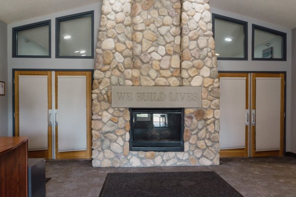 Fireplace with plaque above that says "We Build Lives" located in main lobby area of Avanti