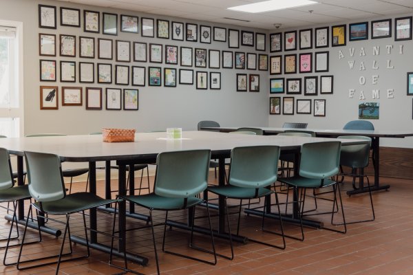 Cafeteria area at Avanti with large table surrounded by chairs, the walls behind feature pictures and writings from past residents that successfully completed the treatment program