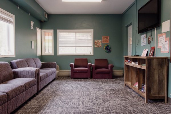 Small lounge room with TV stand and TV on opposite side of two couches and two chairs on the far wall