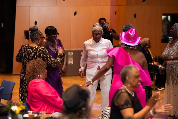 A group of older women in prom attire dancing together on a dance floor