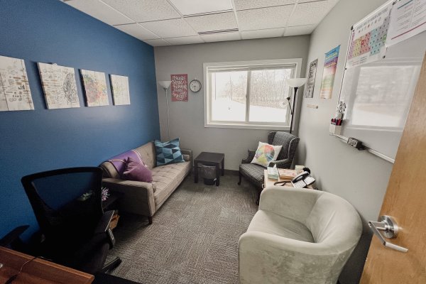 A therapist's office with a couch, two chairs, a desk and a white board on the right wall