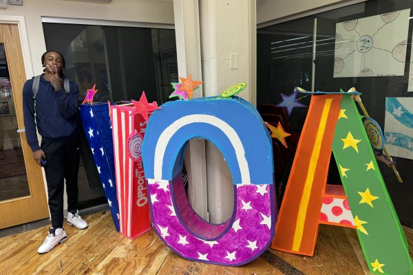 A man stands beside large colorful letters that reads "VOA"