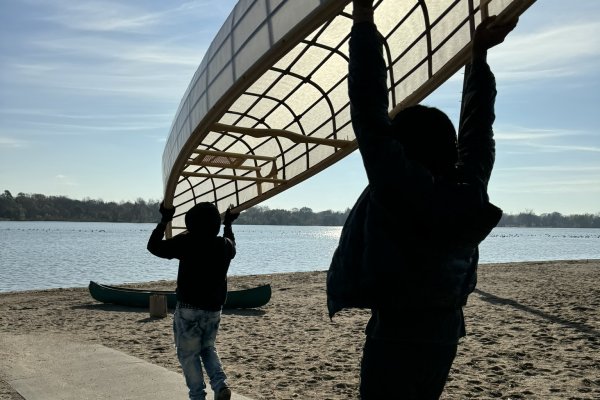 Two people walk towards a lake carrying a canoe above their heads