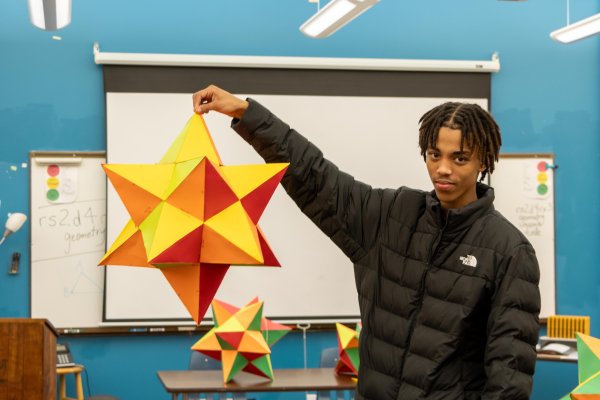 A young man smiles while holding a large paper star in his hands, showcasing his creativity and enthusiasm.